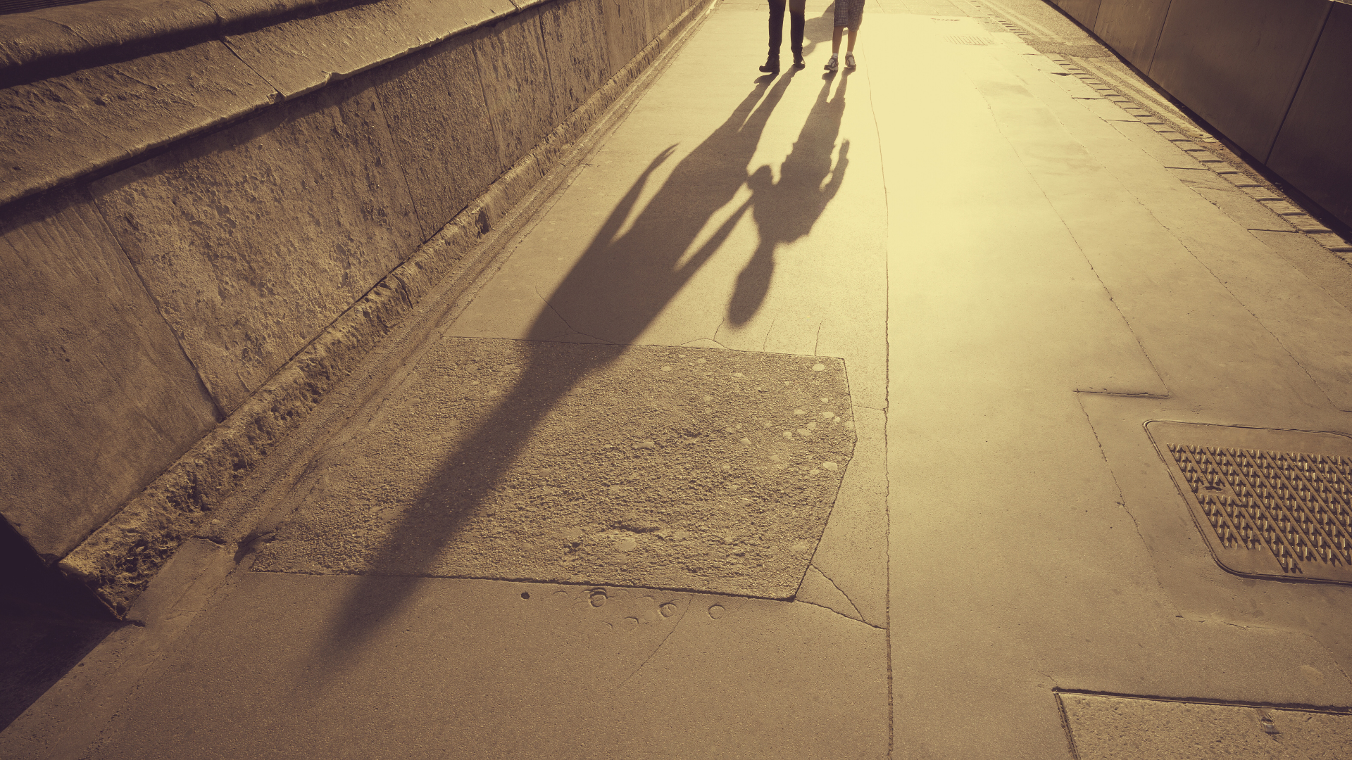 Shadows of two people lengthening on the sidewalk.