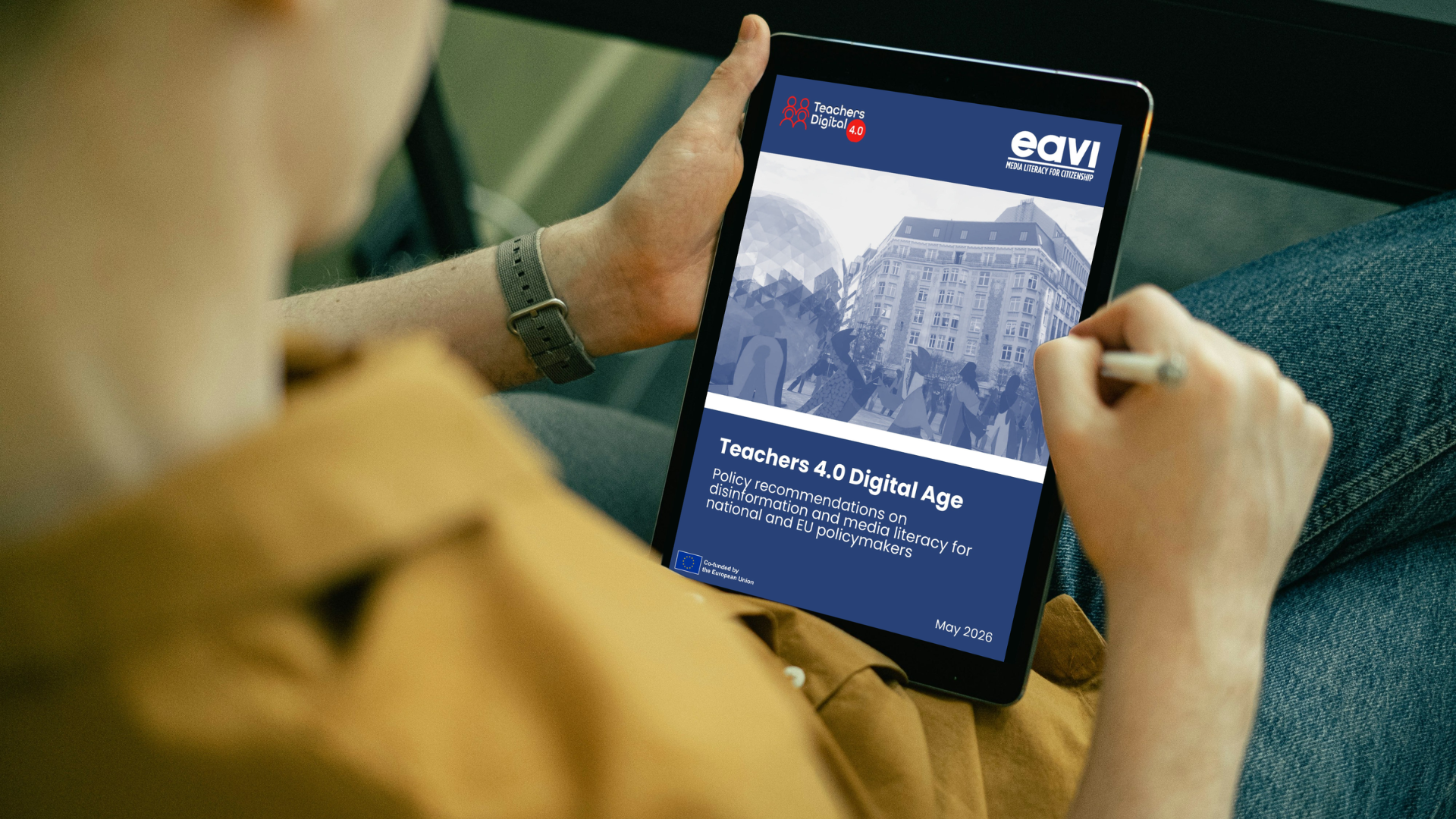 Una persona tiene in mano un tablet che mostra la copertina del documento "Teachers 4.0 Digital Age - Policy recommendations on disinformation and media literacy for national and EU policymakers", pubblicato da EAVI nel maggio 2026